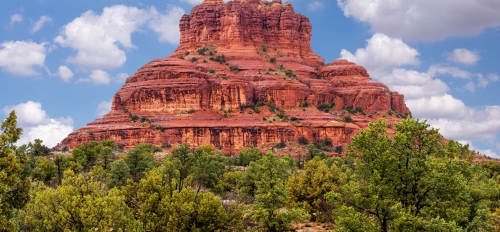 A red rock mountain rises above green trees in Sedona