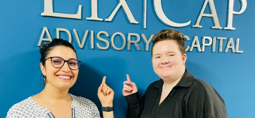 Two people smiling and pointing to a sign on a wall that reads "Lix|Cap Advisory Capital."