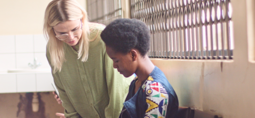 Rachel Thompson wears a green top and glasses as she talks with a student in a patterned shirt in a classroom on campus in Malawi.