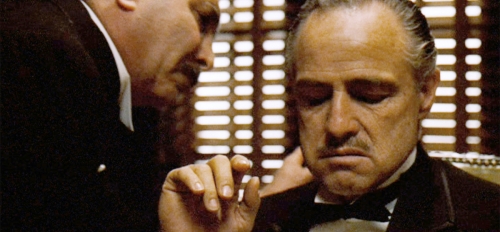 Still from the movie 'The Godfather' depicting a man whispering into the ear of actor Marlon Brando, who portrayed Don Vito Corleone.