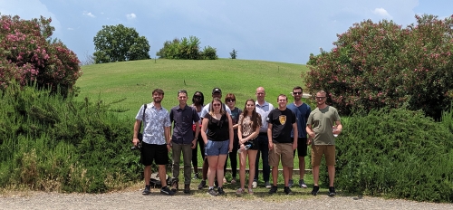 A group of students posing in front of a hill surrounded by greenery.