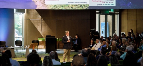 ASU President Michael M. Crow speaks at the Arizona Water Innovation Initiative launch, standing in front of a group of people with a microphone.