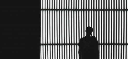 Stock photo of a person's silhouette against a backdrop of iron bars.