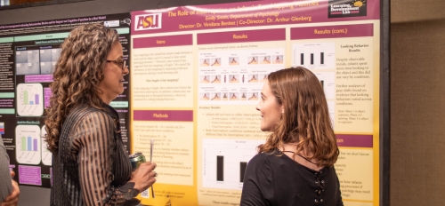 two women speaking in front of a research poster