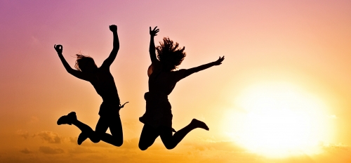 Two people jump for joy as the sun sets behind them.
