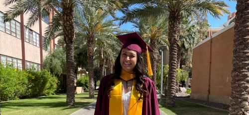 ASU graduate Sami Shah wearing a maroon graduation cap and gown surrounded by palm trees on the Tempe campus.