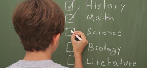 Person writing school subjects on a blackboard