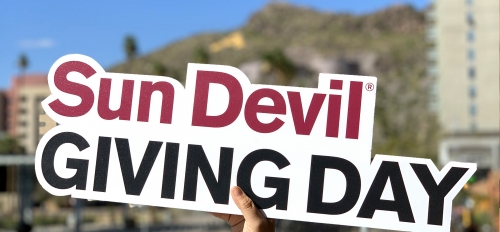 A cutout sign that reads, "Sun Devil Giving Day" is held up in front of Tempe's "A" Mountain in the background.