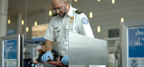 A TSA agent searches luggage at airport security checkpoint.