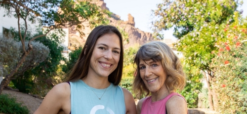 ASU alum Sophie Aigner and her mother, Vickie, pose for a photo on a brick walkway surrounded by greenery and a mountain formation in the background.