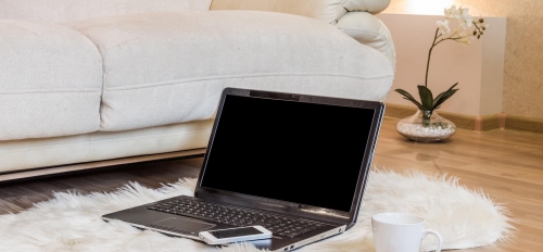 Laptop and iPhone on a rug next to a couch in someone's home.