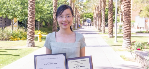 Thu Thao Nguyen, recipient of the 2022 Innovation Award from ASU's School of Molecular Sciences, smiling and holding two plaques on palm walk on the Tempe campus.