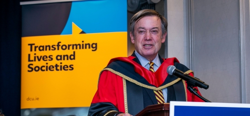ASU President Michael Crow speaks behind a lectern with a DCU sign on the front.