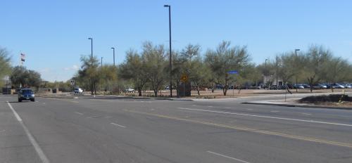 A wide street with a car in the distance driving toward the vantage point.