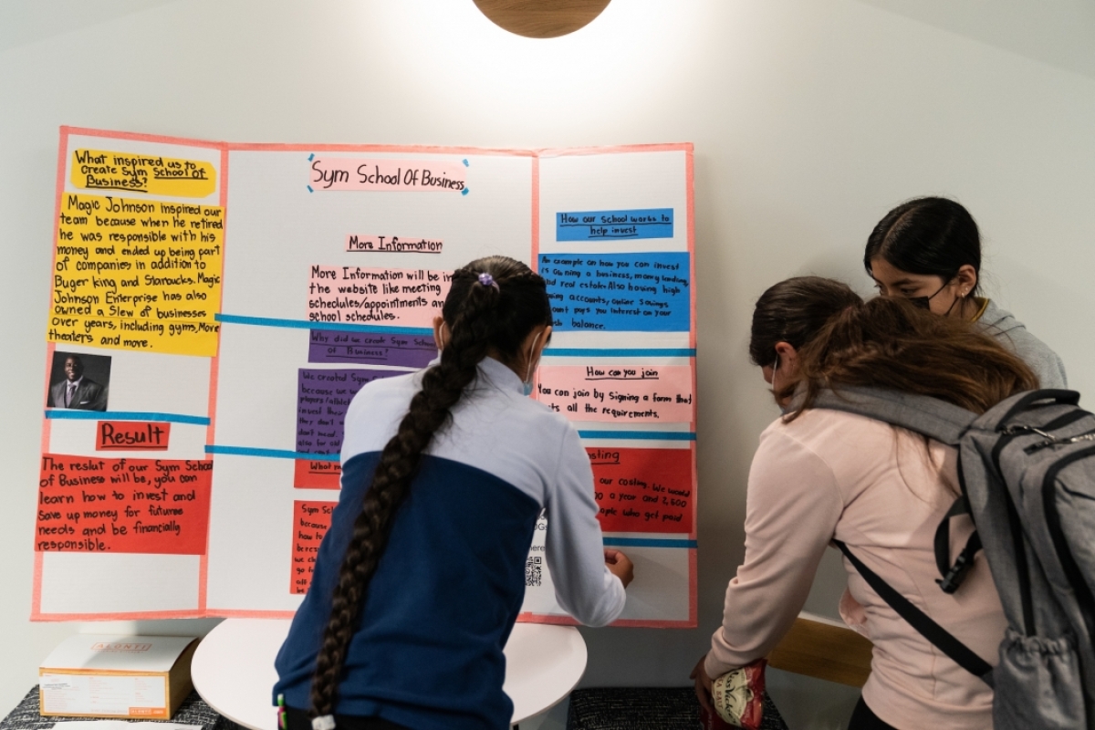 Three middle school students set up a poster board on a table.