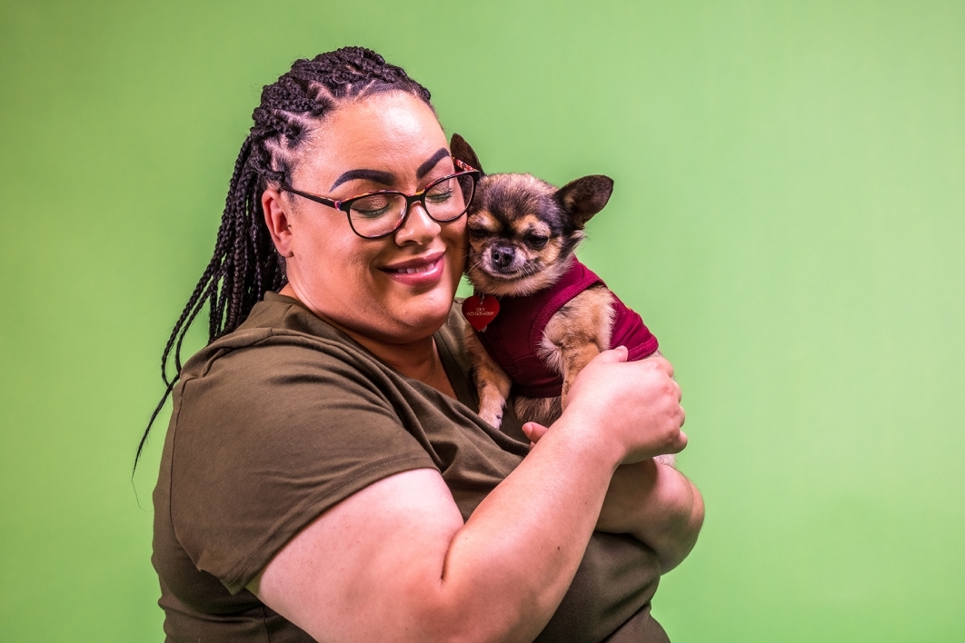 portrait of woman holding a small pug-mix dog against a green background