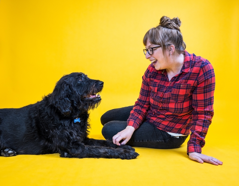 woman smiling at large black dog against yellow background