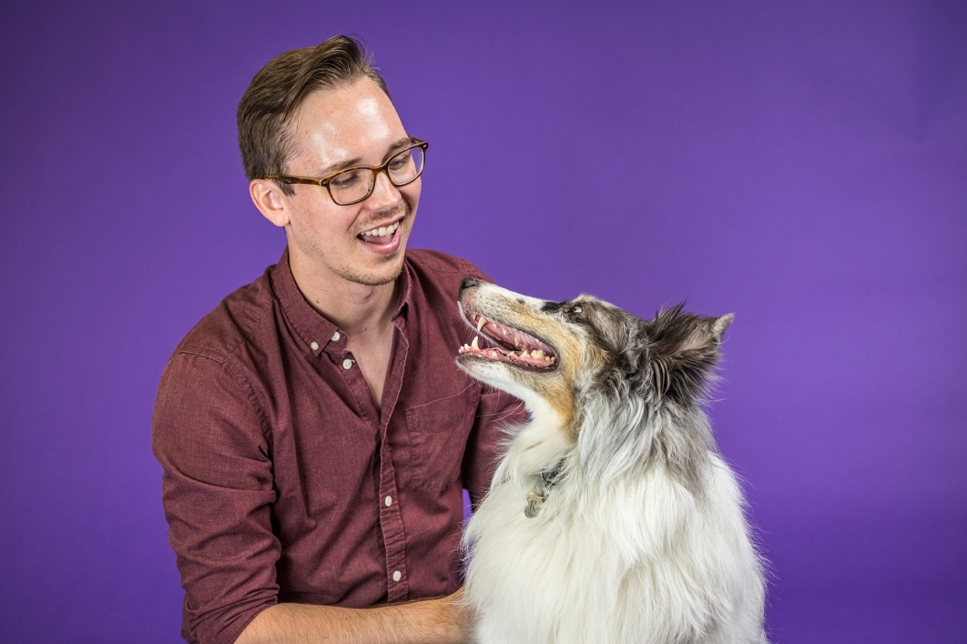 man smiling at collie dog against a purple background