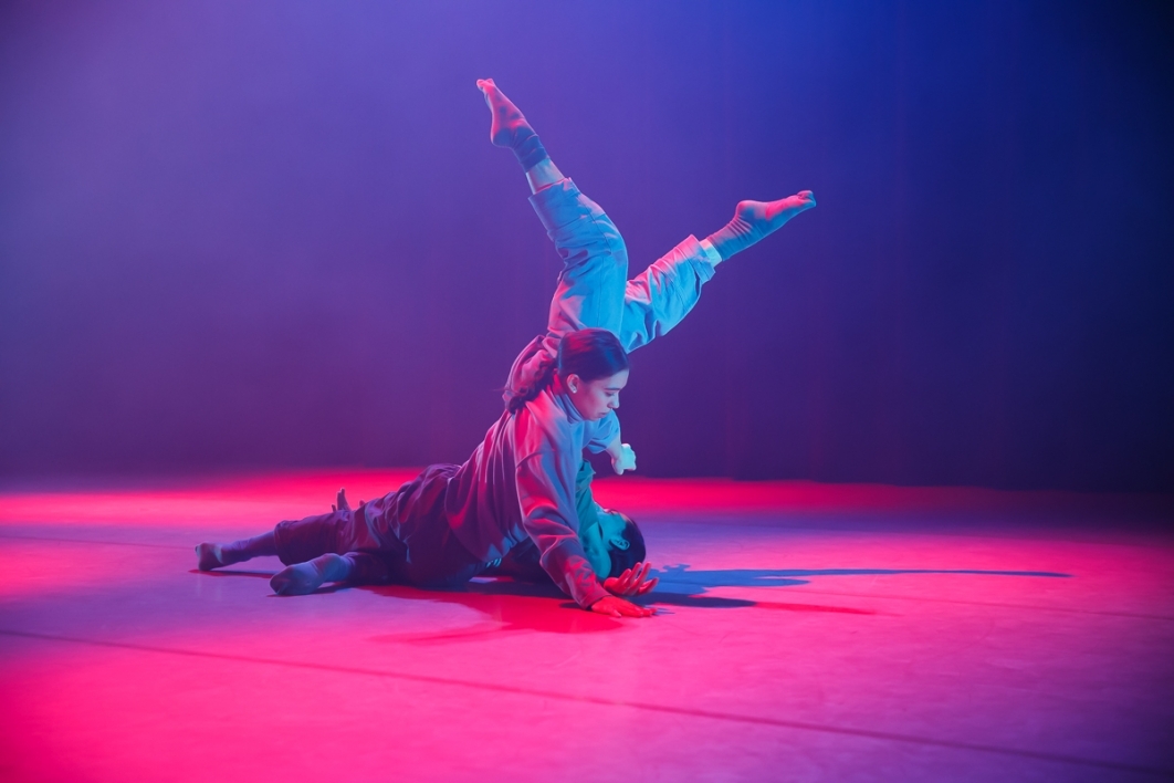 Dancer mid-performance on a stage surrounding by colorful lighting.