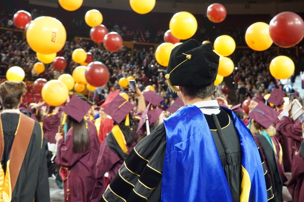 A professor looks on while balloons fall on the graduates at Watts College's fall 2023 convocation.