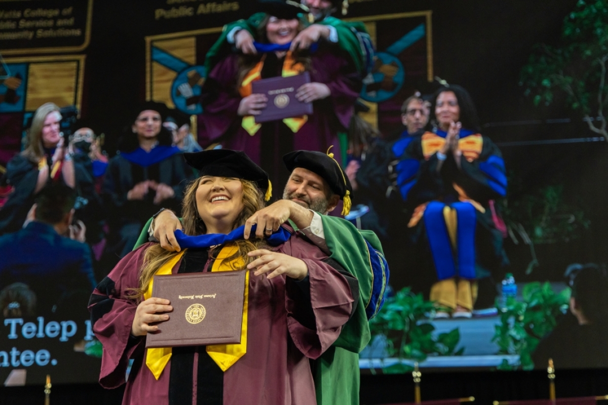 Associate Dean Cody Telep helps doctoral candidate with her hood, spring 2023 convocation