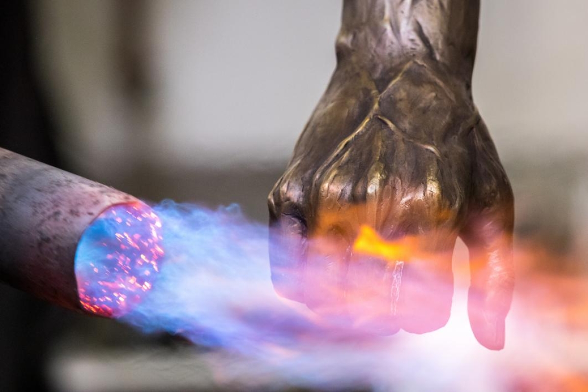 A blowtorch applies a patine to a bronze statue's hand