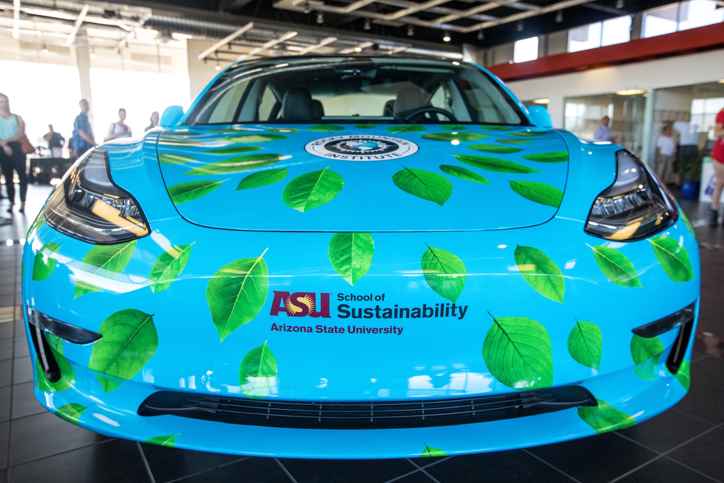 blue-colored wrap with green leaves and the ASU School of Sustainability logo on a Tesla car