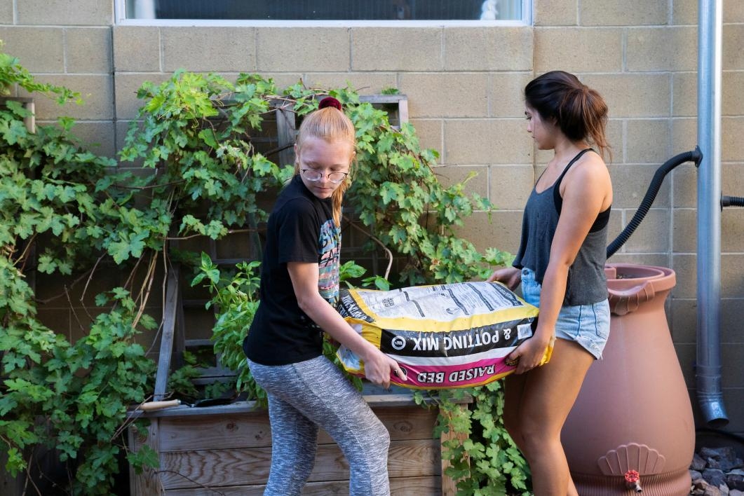 Two girls carry a bag of dirt to a garden