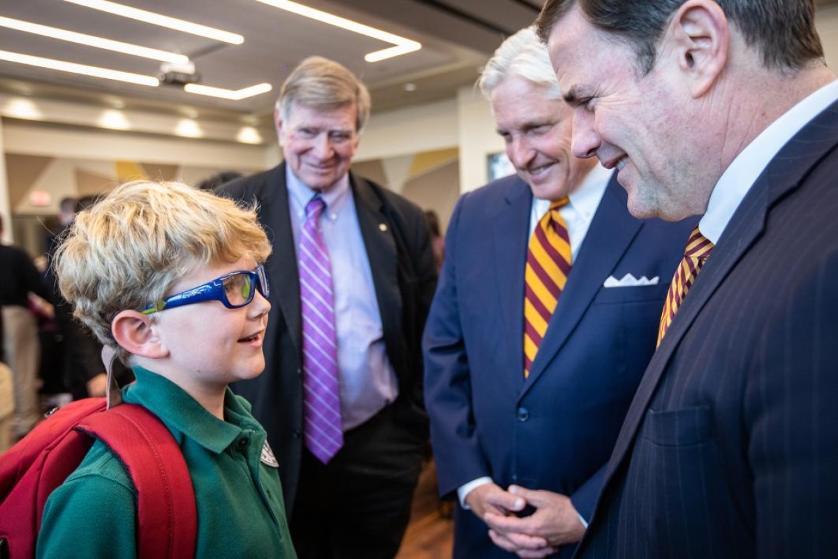 governor Doug Ducey speaks to a child at the greek leadership village opening