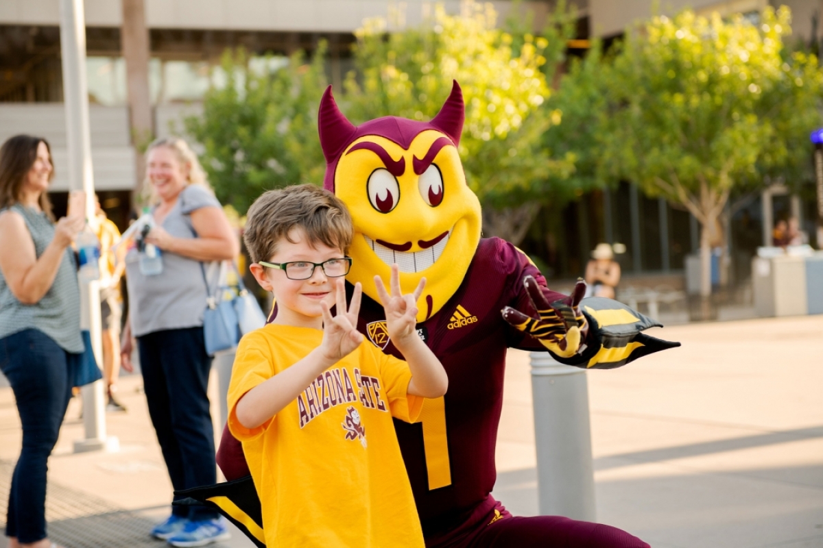 A young boy does pitchforks with both hands as he gets a photo with Sparky