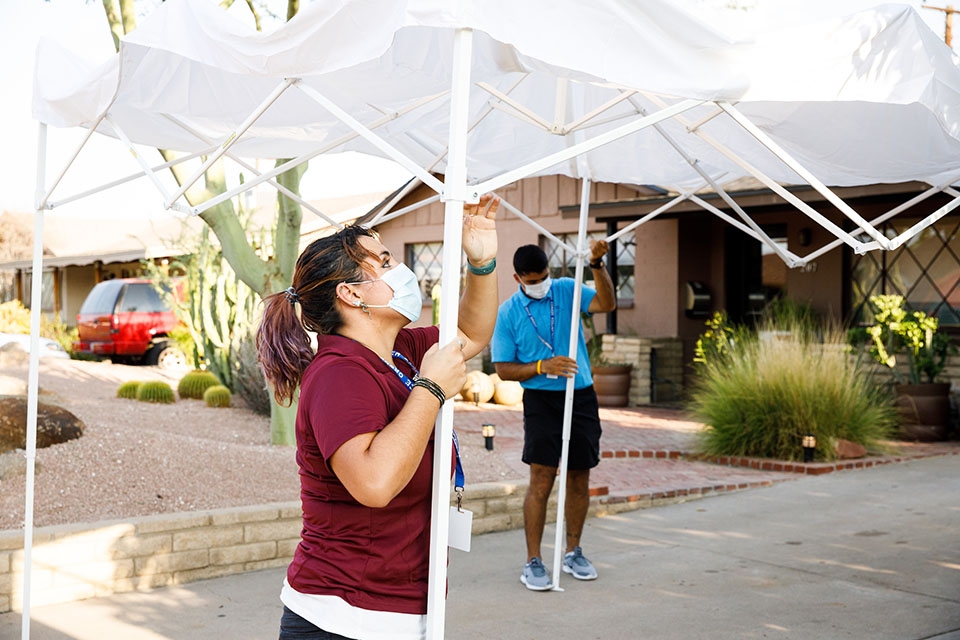 Two volunteers set up a collapsible tent in the driveway of an Arizona home.