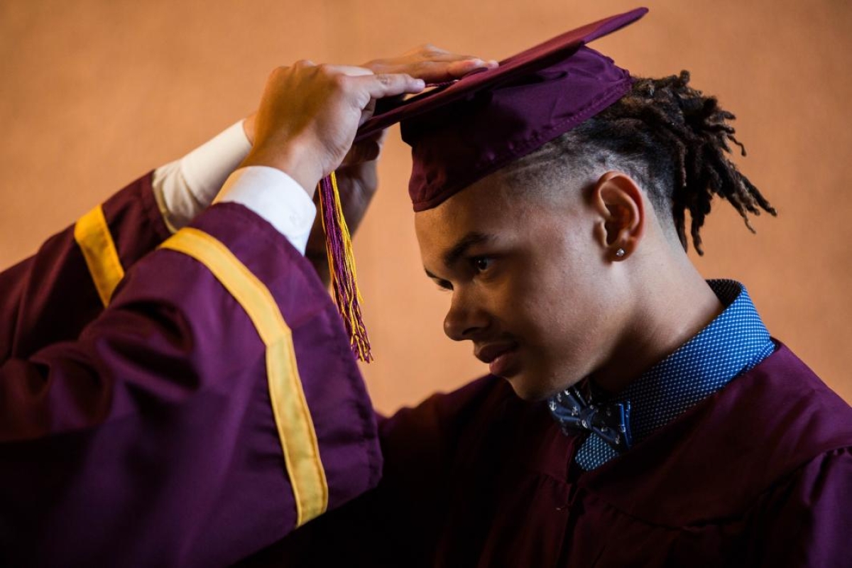 A student adjusts his graduation cap.