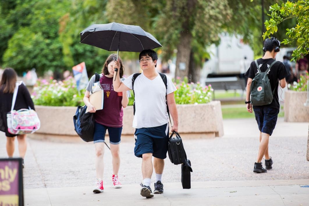 two students walking on campus carrying umbrella