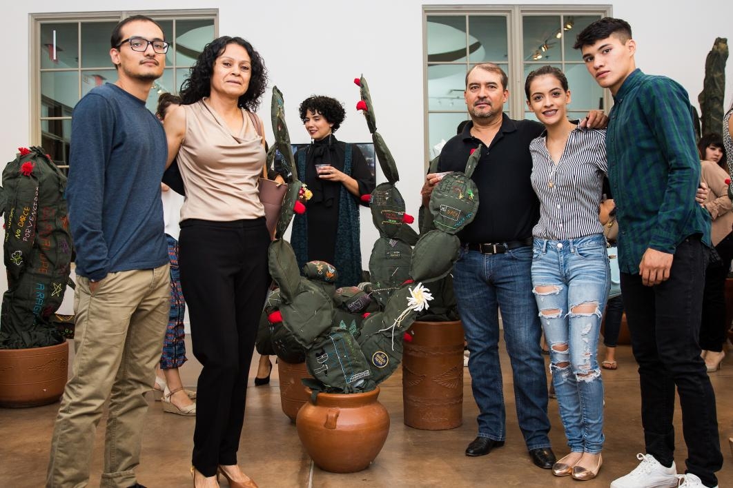 A family poses with a cloth cactus embroidered with their immigration story.
