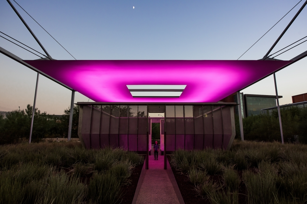 An outdoor art installation glows pinkish purple