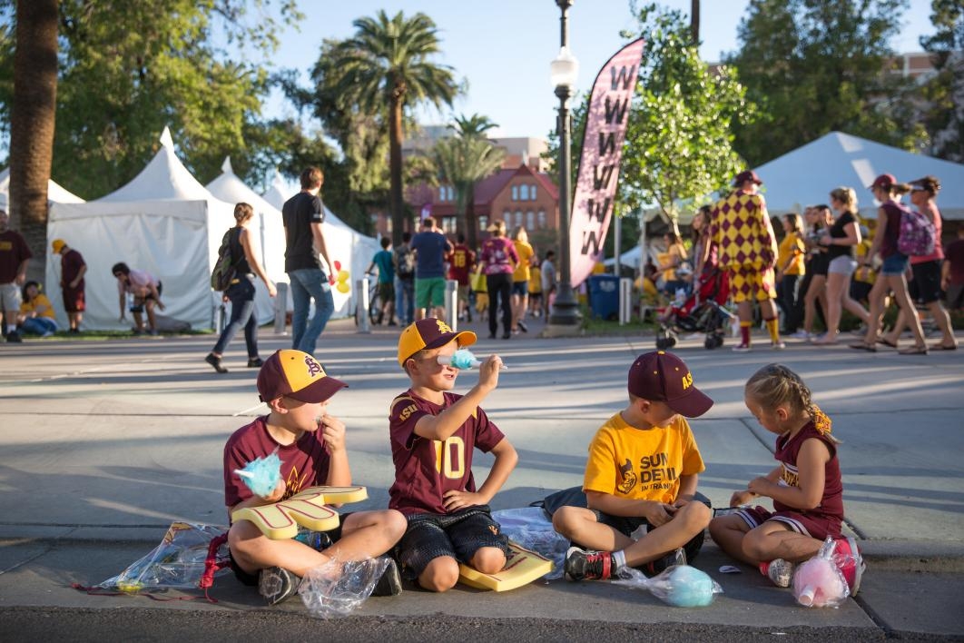 Children sitting on a sidewalk wearing maroon and gold clothing during ASU's Homecoming Parade.