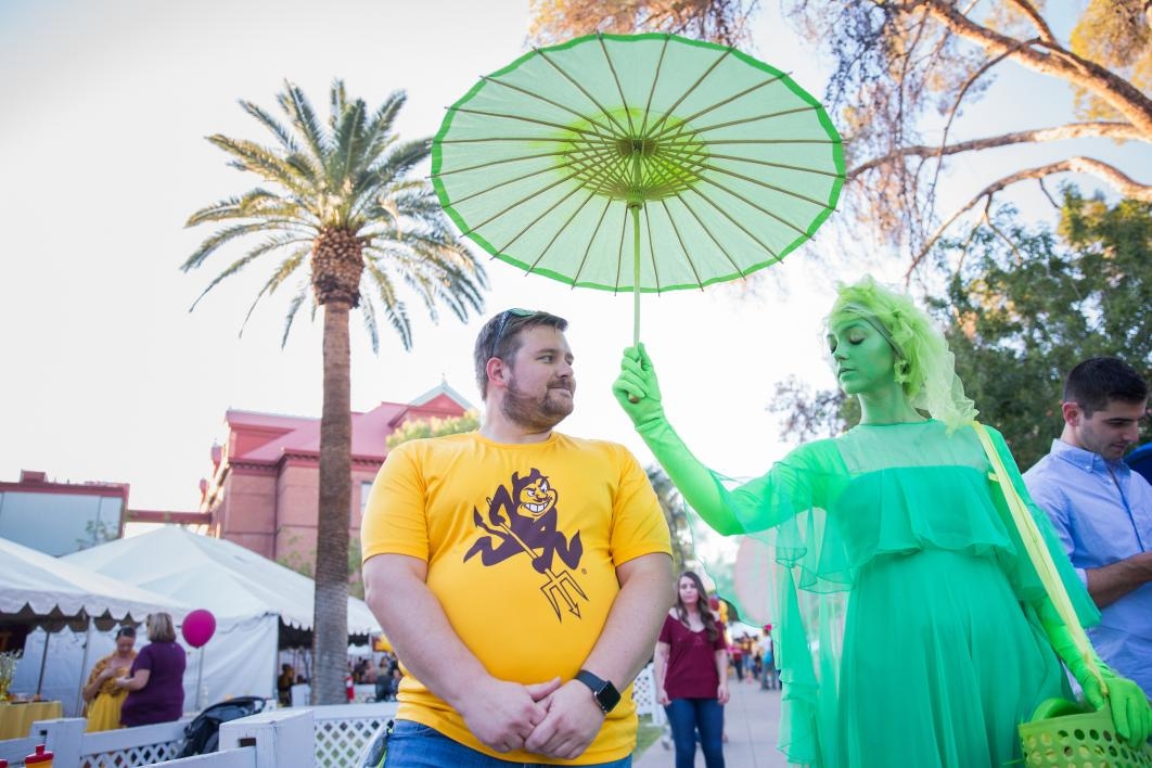 woman dressed in green costume holding umbrella over man