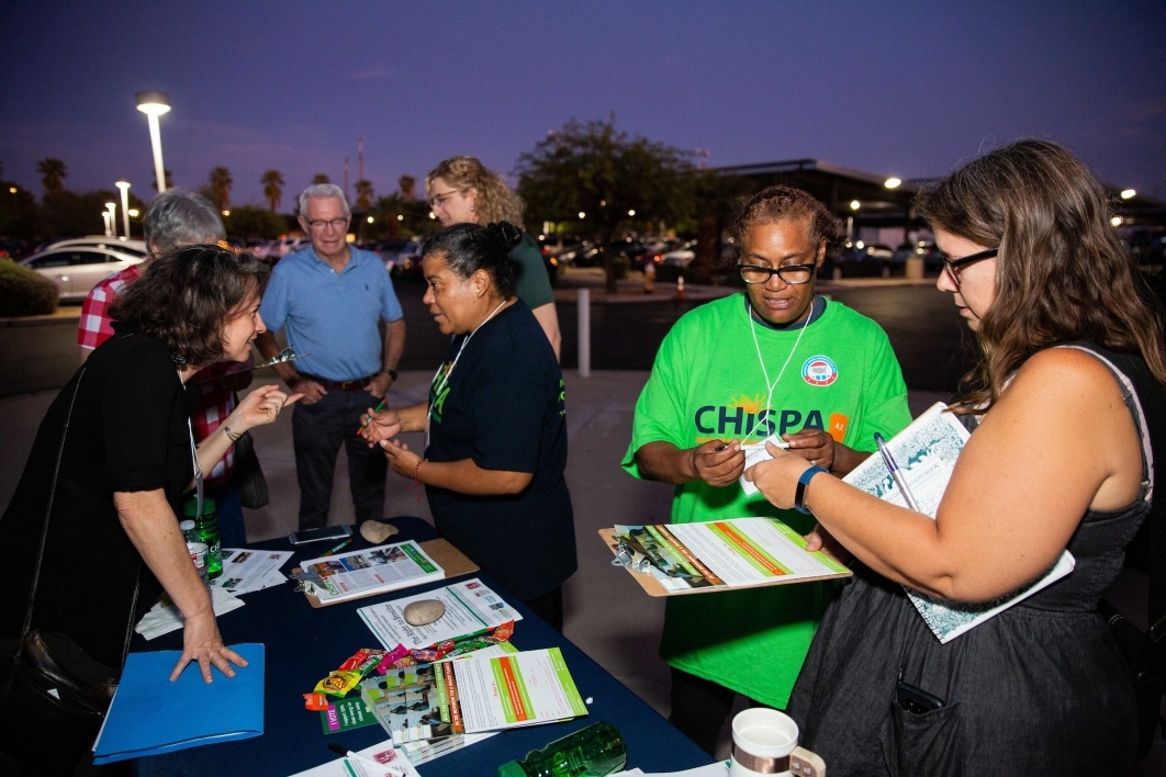 A CHISPA AZ representative speaks to visitors at an outdoor table