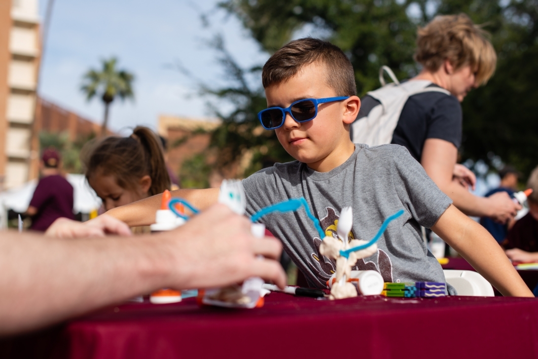 child in sunglasses makes a craft at homecoming block party