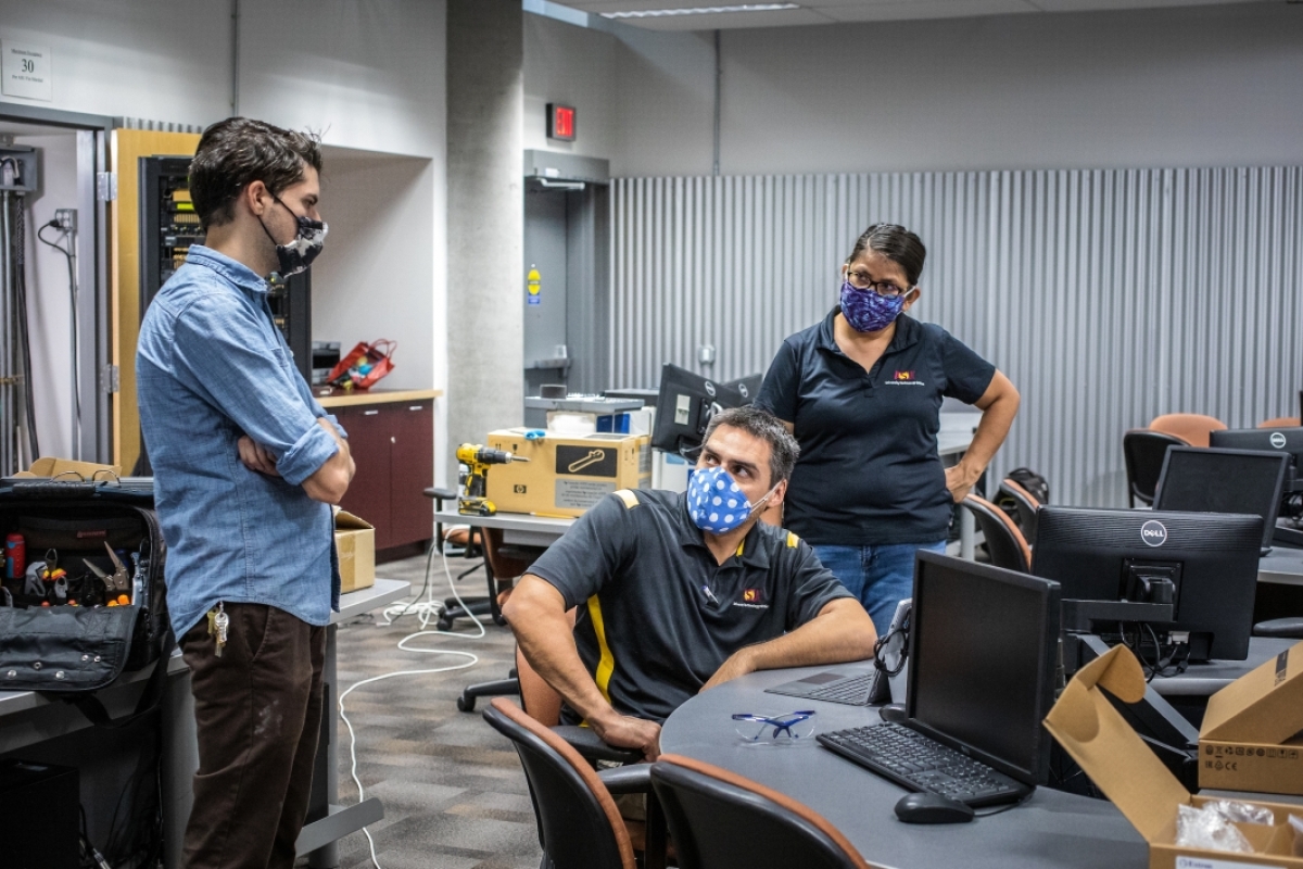 Two men and a woman discuss an AV classroom setup while wearing masks