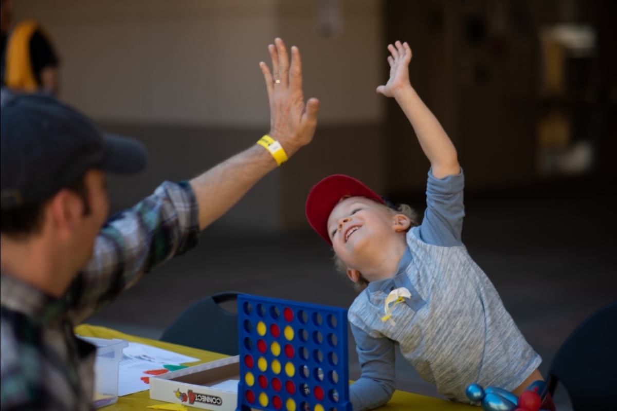 little boy wearing a hat high fives his dad playing connect four