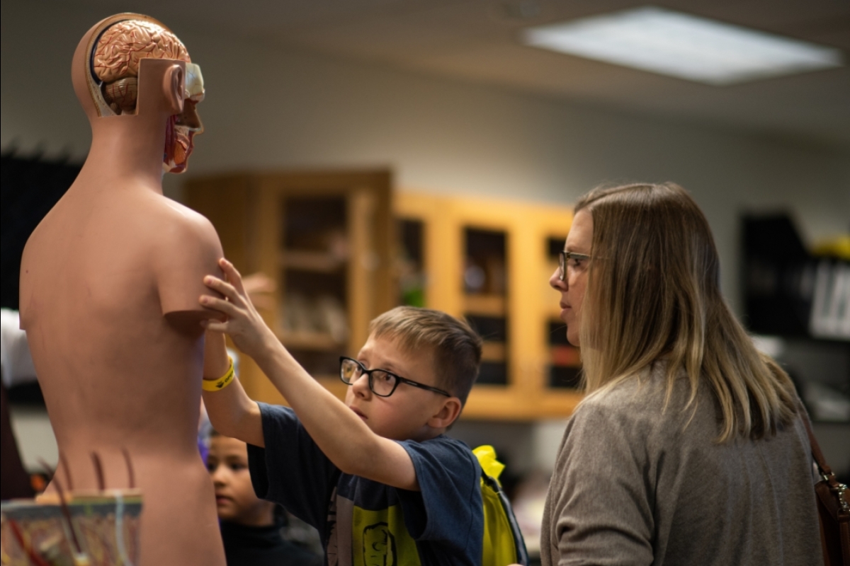 young boy in glasses replaces parts on an anatomy of a human dummy