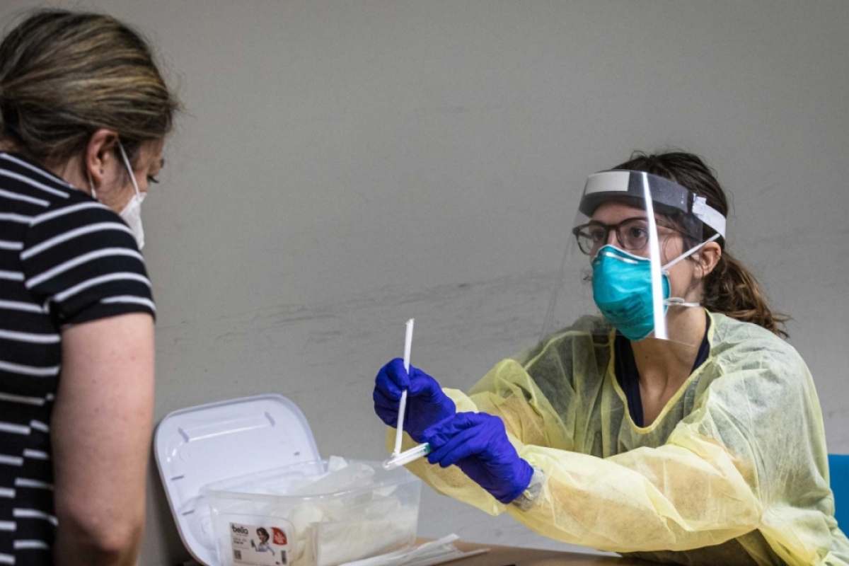 A woman in PPE hands a COVID test kit to a woman wearing a mask