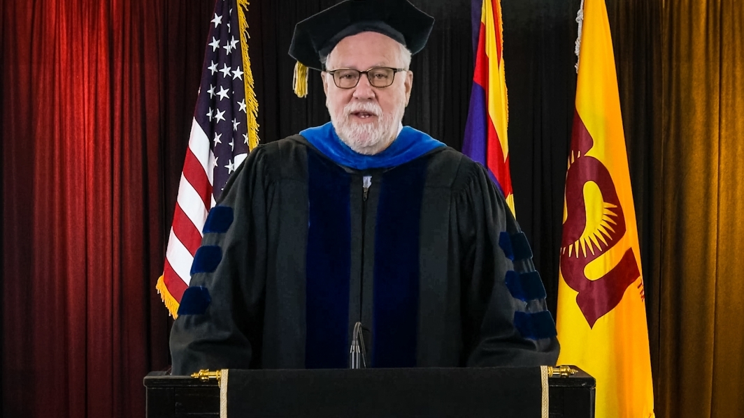 ASU Provost Mark Searle speaks at a lectern in front of flags