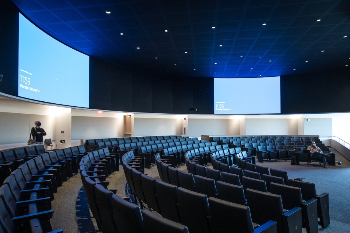 An auditorium with curving rows of seats and several large screens