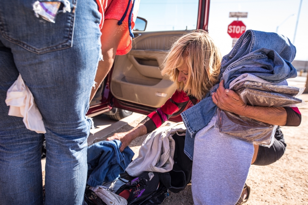 A homeless woman searches through a bag of clothing next to a van