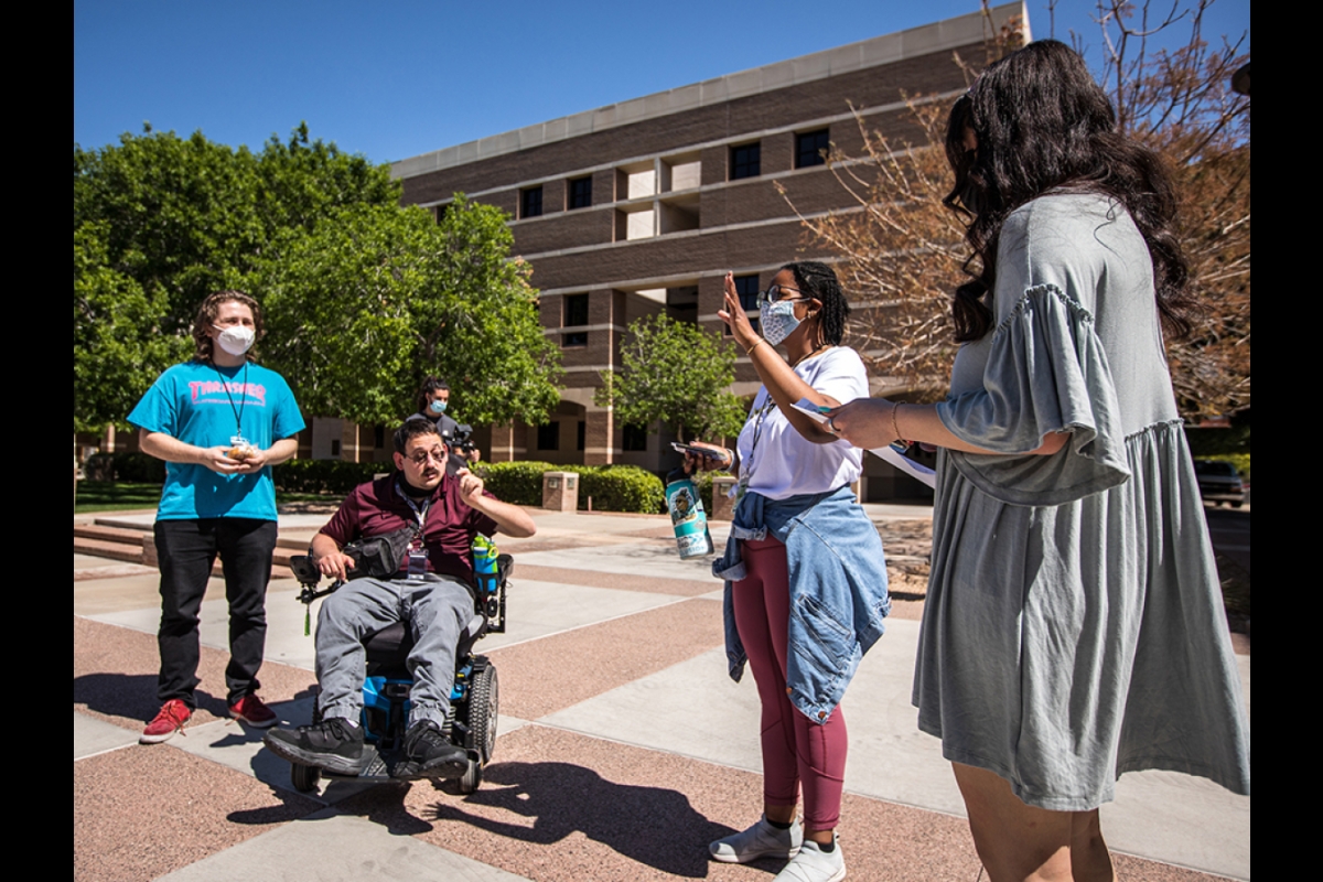 three people standing outside with one person in the middle in a wheelchair