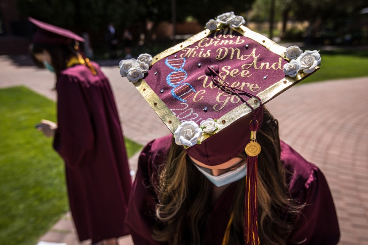 A woman tilts her head forward so the wording on her graduation cap can be read: I'll climb this DNA and see where I can go