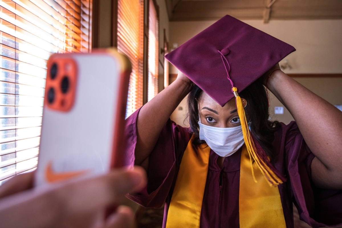 A woman checks the placement of her graduation cap in a phone being held by someone else