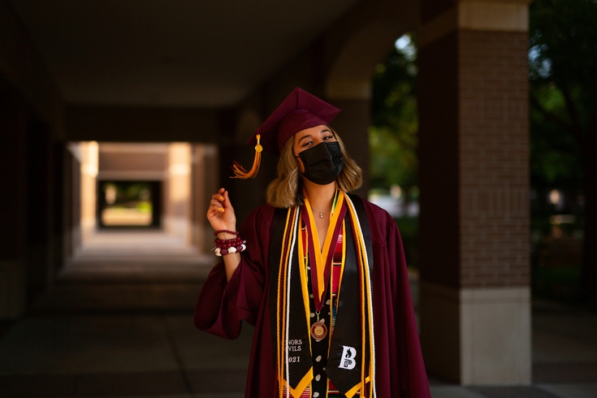 woman wearing a mask and a cap and gown standing in a hallway